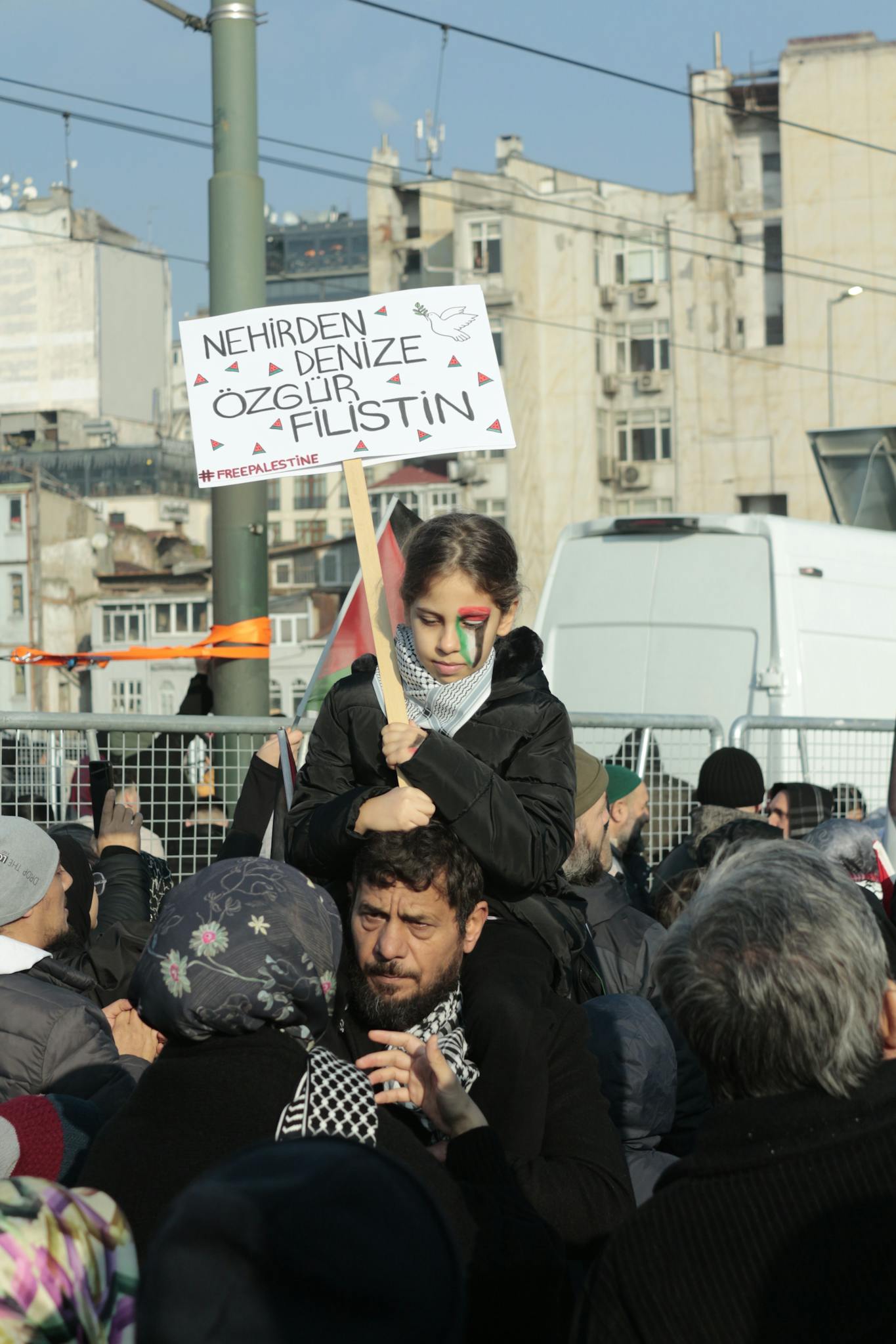 People gather for a Palestinian freedom protest in a city environment, holding signs.