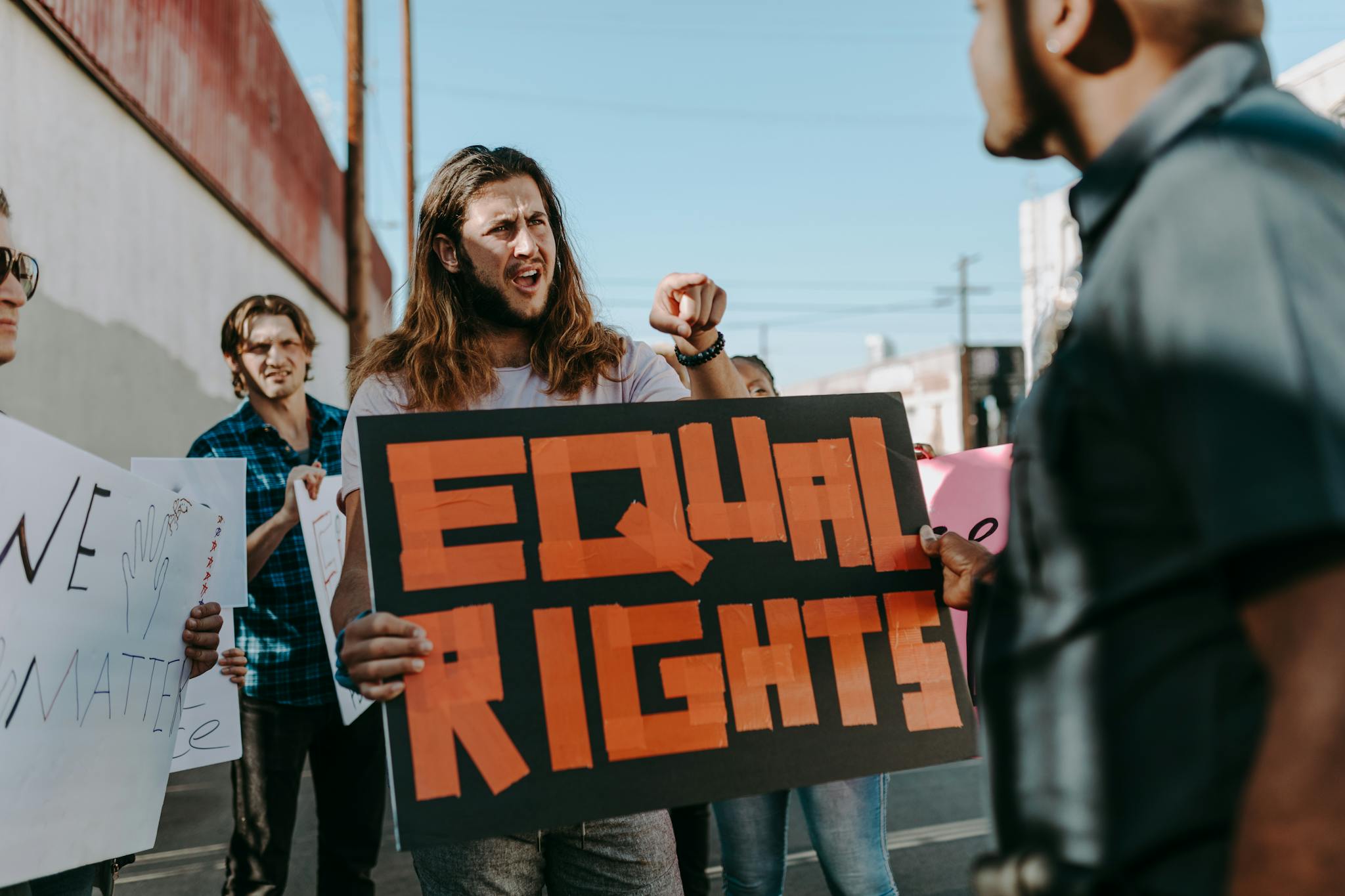 Protesters holding signs advocating equal rights during a rally on a sunny day.